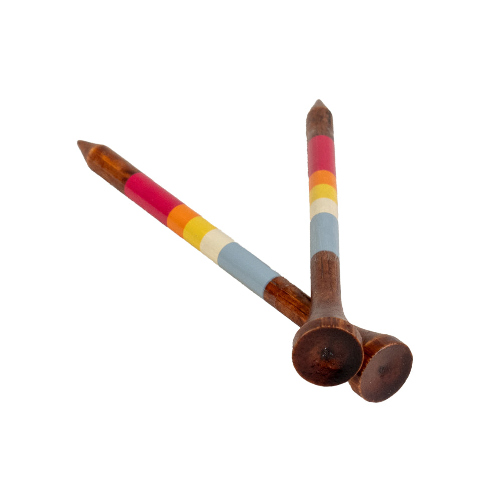 Two bamboo golf tees rest crossed together, each showing the same burgundy, orange, cream, and dusty blue gradient stripes.