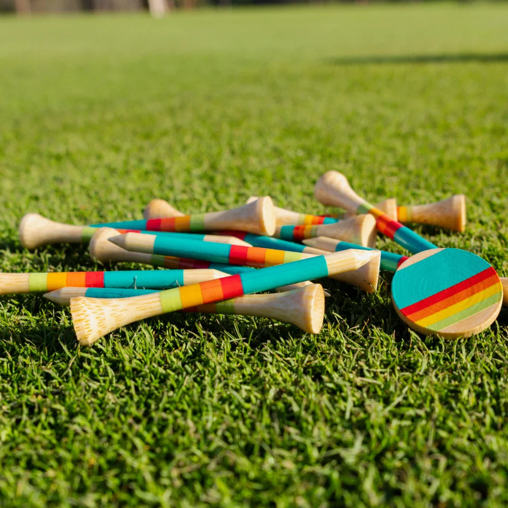 A pile of sunrise gradient bamboo golf tees and ball markers rests on a grass field.