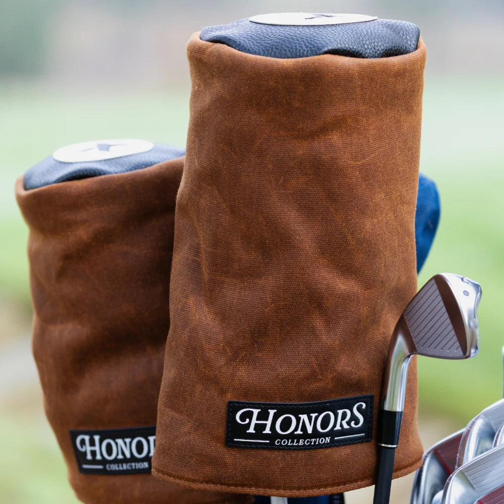 Two waxed canvas Barrel Fairway Wood Headcovers sit in a golf bag next to an iron club.