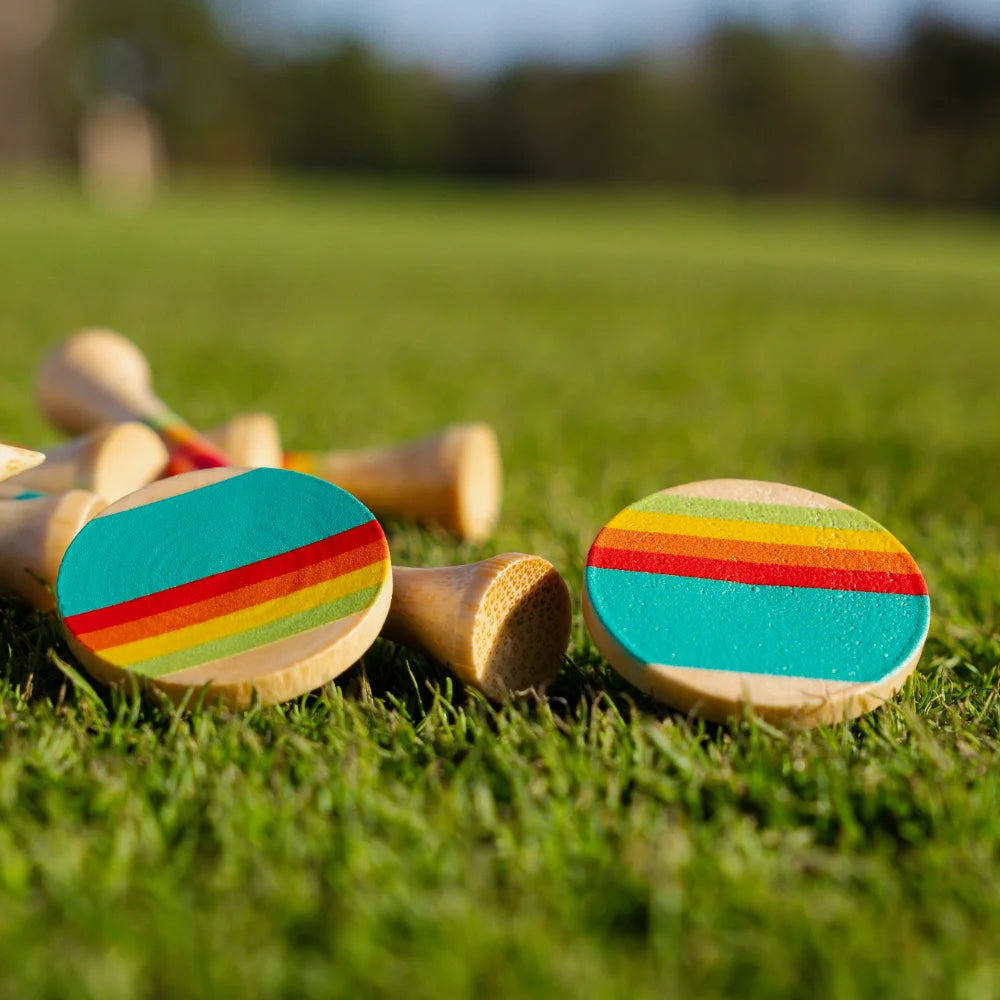 Close-up of two sunrise gradient ball markers on grass, with matching bamboo tees blurred in the background.